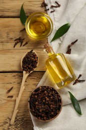Essential oil and dried cloves on wooden table, flat lay