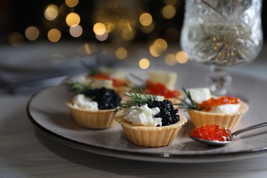 Photo of Delicious tartlets with red and black caviar served on white wooden table against blurred festive lights, closeup. Space for text
