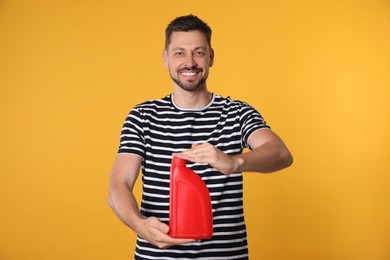 Man holding red container of motor oil on orange background