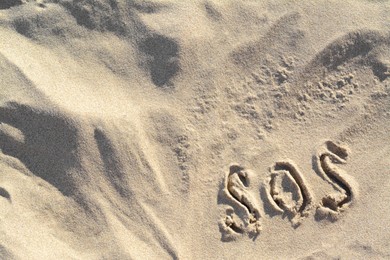 SOS message written on sandy beach outdoors, top view. Space for text