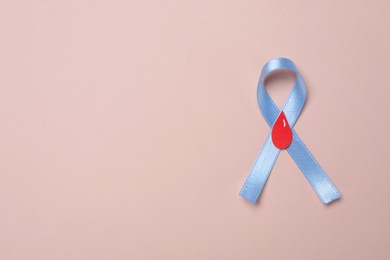 Light blue ribbon with paper blood drop on pale pink background, top view and space for text. Diabetes awareness