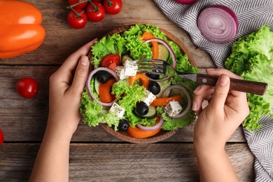 Woman eating tasty fresh Greek salad at wooden table, top view
