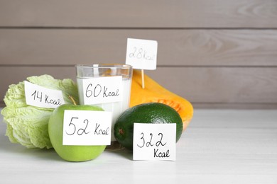 Food products with calorific value tags on white wooden table, space for text. Weight loss concept