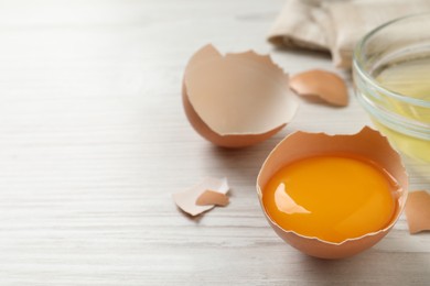 Photo of Raw yolk in broken chicken eggshell on wooden table, closeup. Space for text