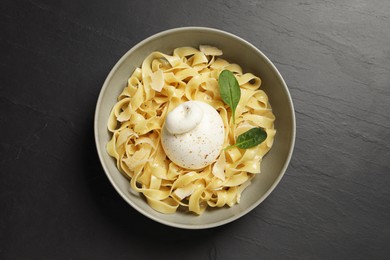 Delicious pasta with burrata cheese and basil on black table, top view