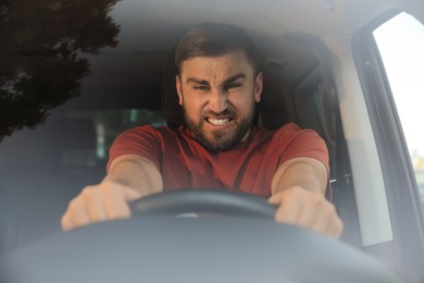 Photo of Emotional man in car, view through windshield. Aggressive driving behavior