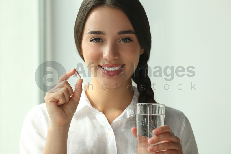 Young woman with glass of water and dietary supplement pill indoors