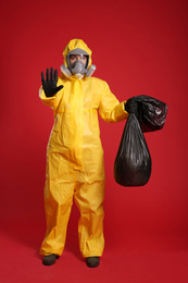 Woman in chemical protective suit holding trash bag on red background. Virus research