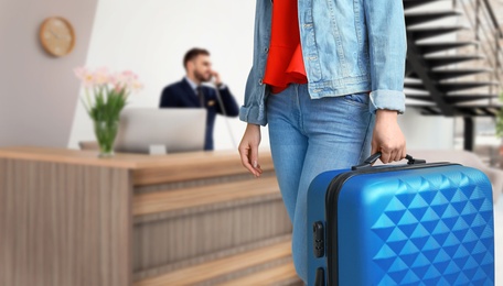 Woman with suitcase near receptionist in hotel, closeup view