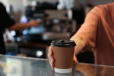 Photo of Barista putting takeaway paper cup with coffee on countertop in cafe, closeup