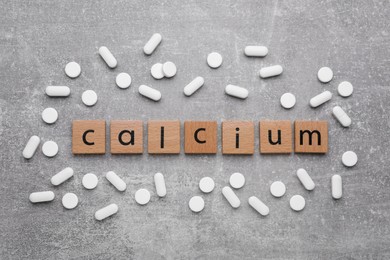 Word Calcium made of cubes with letters and pills on gray background, top view