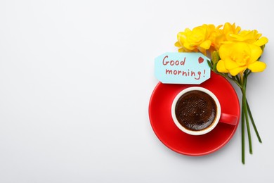 Photo of Cup of aromatic coffee, beautiful yellow freesias and Good Morning note on white background, flat lay. Space for text