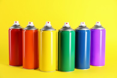 Photo of Colorful cans of spray paints on yellow background