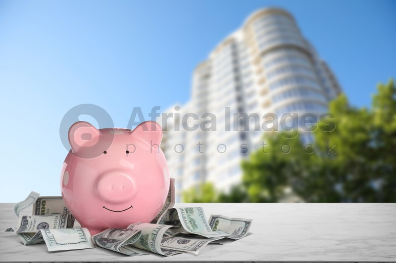Piggy bank and money on stone surface and blurred view of beautiful skyscraper, space for text. Mortgage concept