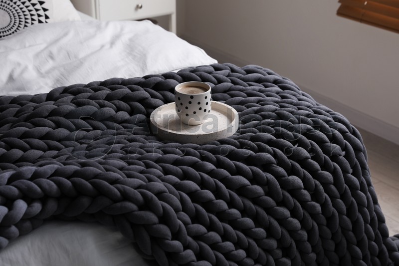 Tray with cup of coffee and soft chunky knit blanket on bed indoors