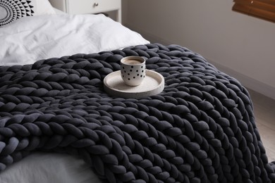 Photo of Tray with cup of coffee and soft chunky knit blanket on bed indoors