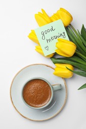 Cup of aromatic coffee, beautiful yellow tulips and Good Morning note on white background, flat lay