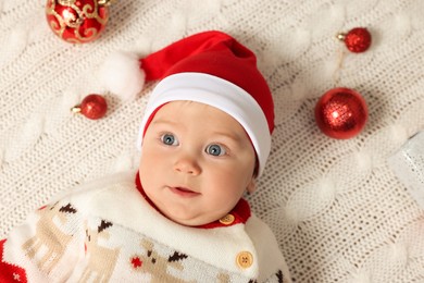 Cute little baby in Christmas outfit surrounded by  baubles on white knitted plaid, top view. Winter holiday