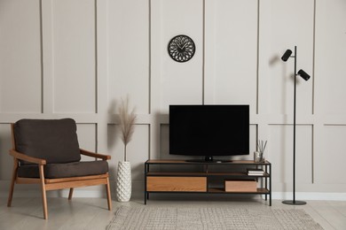 Photo of Elegant room interior with modern TV on stand, armchair and floor lamp