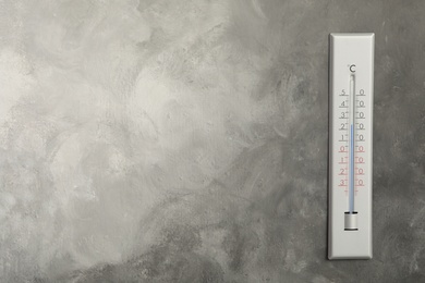 Weather thermometer on grey wall. Space for text