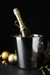 Happy New Year! Bottle of sparkling wine in bucket and festive decor on table against black background