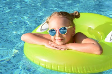 Happy little girl with inflatable ring in outdoor swimming pool on sunny day