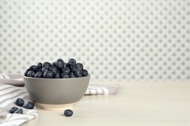 Ceramic bowl with blueberries on white wooden table, space for text. Cooking utensil