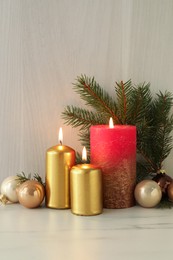 Burning candles with Christmas baubles and fir tree branch on table against wooden background