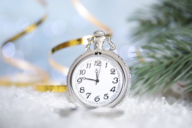 Pocket watch, golden serpentine streamers and fir branch on snow against blurred lights. New Year countdown
