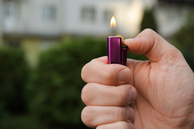 Man holding lighter with burning flame outdoors, closeup. Space for text