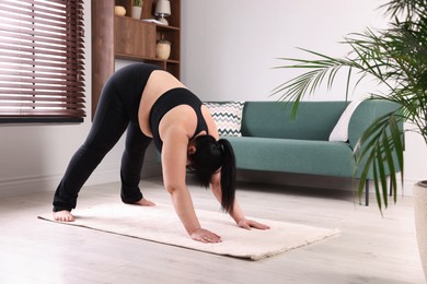Overweight mature woman practicing yoga on rug at home