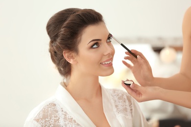Makeup artist preparing bride before her wedding indoors