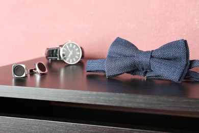 Stylish blue bow tie, cufflinks and wristwatch on wooden table