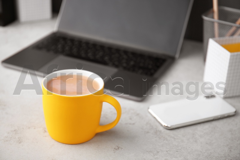 Yellow cup with coffee and phone near laptop on office table. Break time