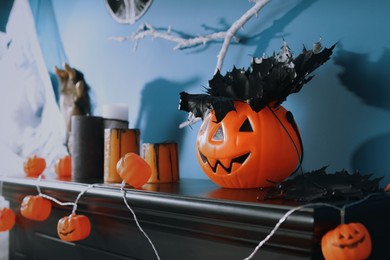 Photo of Jack-o'-lantern lights and black maple leaves on wooden fireplace near blue wall