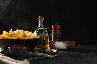 Photo of Composition with bowl of steaming baked potatoes, sauce and spices on black table