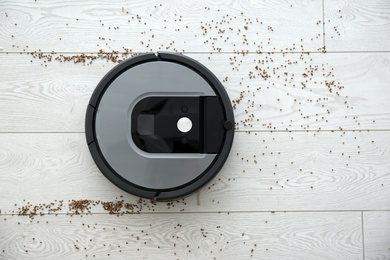 Modern robotic vacuum cleaner removing scattered buckwheat from wooden floor, top view