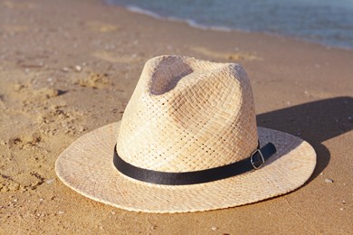 Stylish straw hat on sandy beach near sea