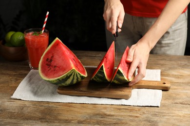 Woman cutting delicious watermelon at wooden table against dark background, closeup