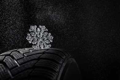 Winter tire with icy snowflake on black background, closeup. Space for text