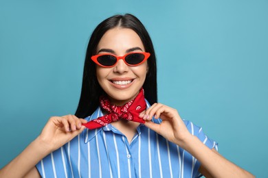 Fashionable young woman in stylish outfit with bandana on light blue background