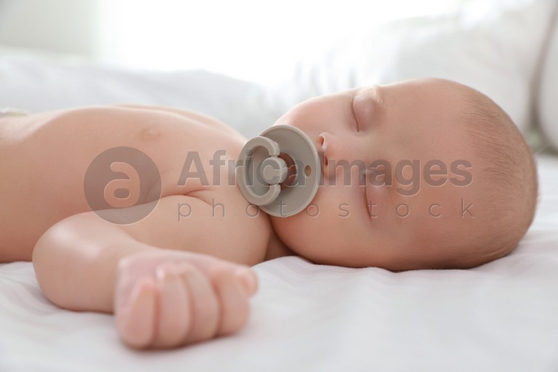 Cute little baby with pacifier sleeping on bed, closeup