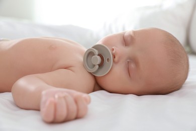 Cute little baby with pacifier sleeping on bed, closeup