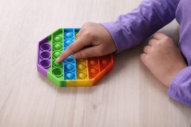 Little child playing with pop it fidget toy at wooden table, closeup