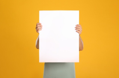 Man holding white blank poster on yellow background. Mockup for design
