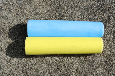 Yellow and light blue chalk sticks on asphalt, flat lay