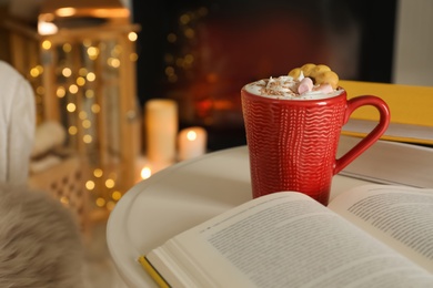 Cup of cocoa, book and cookie on white table indoors