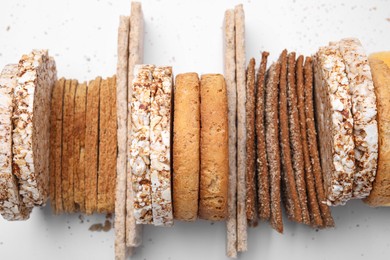 Many fresh rye crispbreads, crunchy rice cakes and rusks on white background, top view