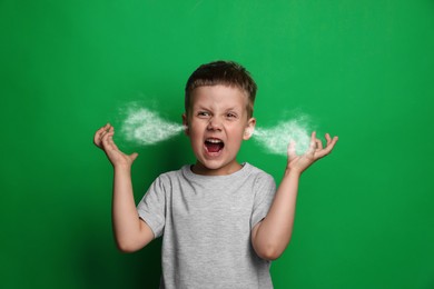 Aggressive little boy with steam coming out of his ears on green background