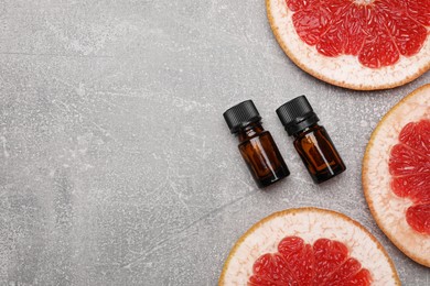 Bottles of essential oil with grapefruit slices on grey table, flat lay. Space for text